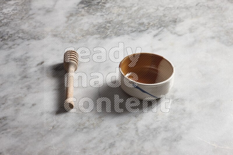 Multicolored pottery bowl with wooden honey dipper on the side on grey marble background
