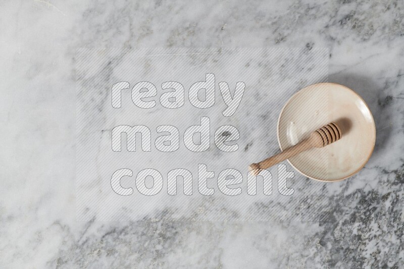 طبق فخاري بيج مع ملعقة عسل خشبية بداخله على خلفية من الرخام الرمادي