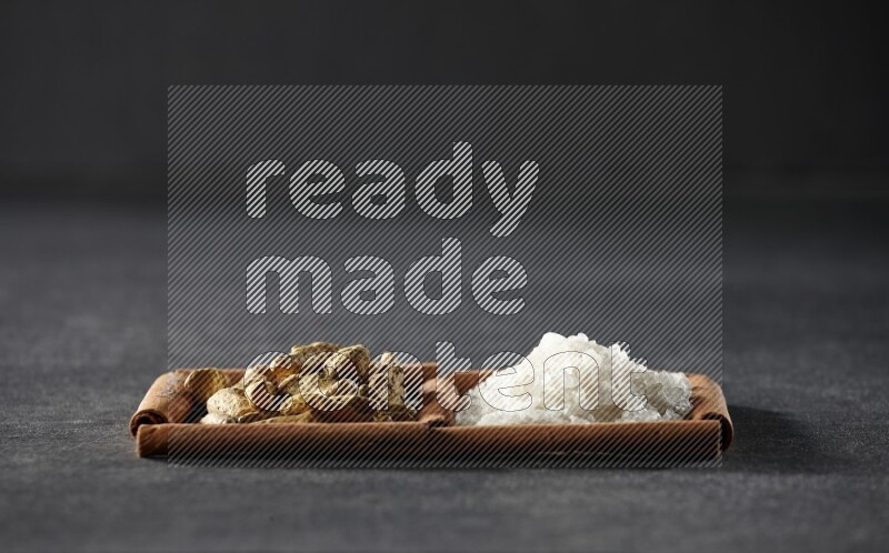 مربعان من أعواد القرفة ممتلئان بالملح الأبيض وأصابع الكركم علي خلفية سوداء