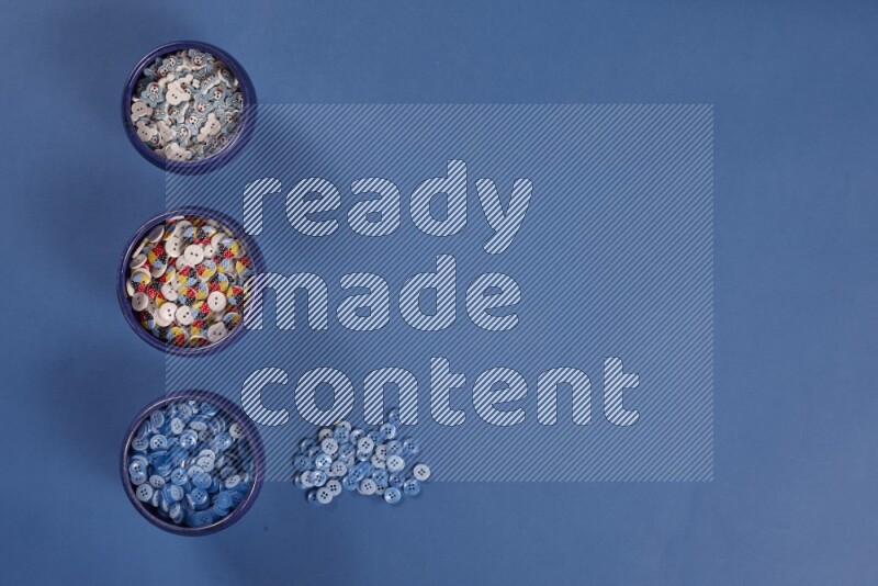 أوعية فخارية متعددة الألوان مليئة بالأزرار الملونة على خلفية زرقاء