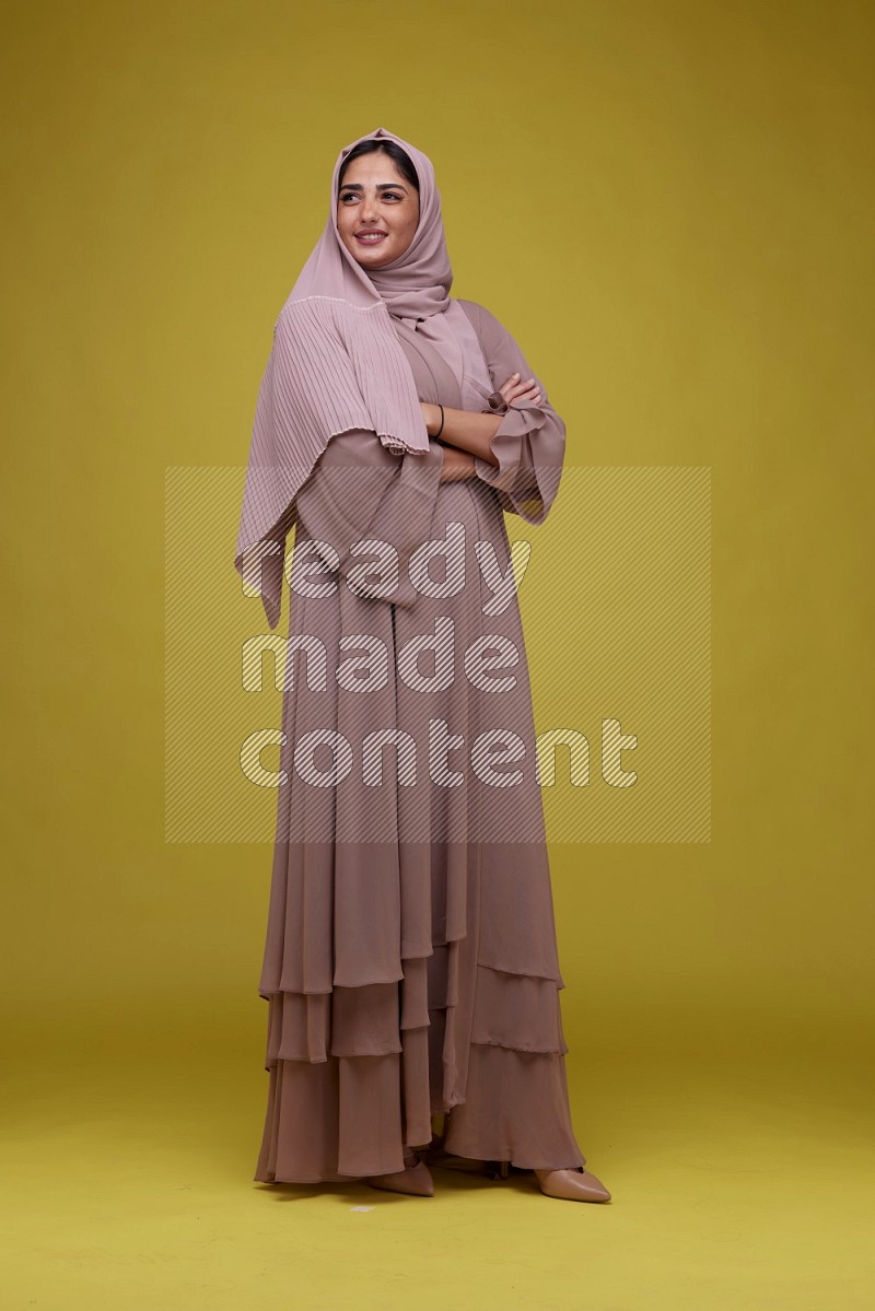 A woman Posing on a Yellow Background wearing Brown Abaya with Hijab