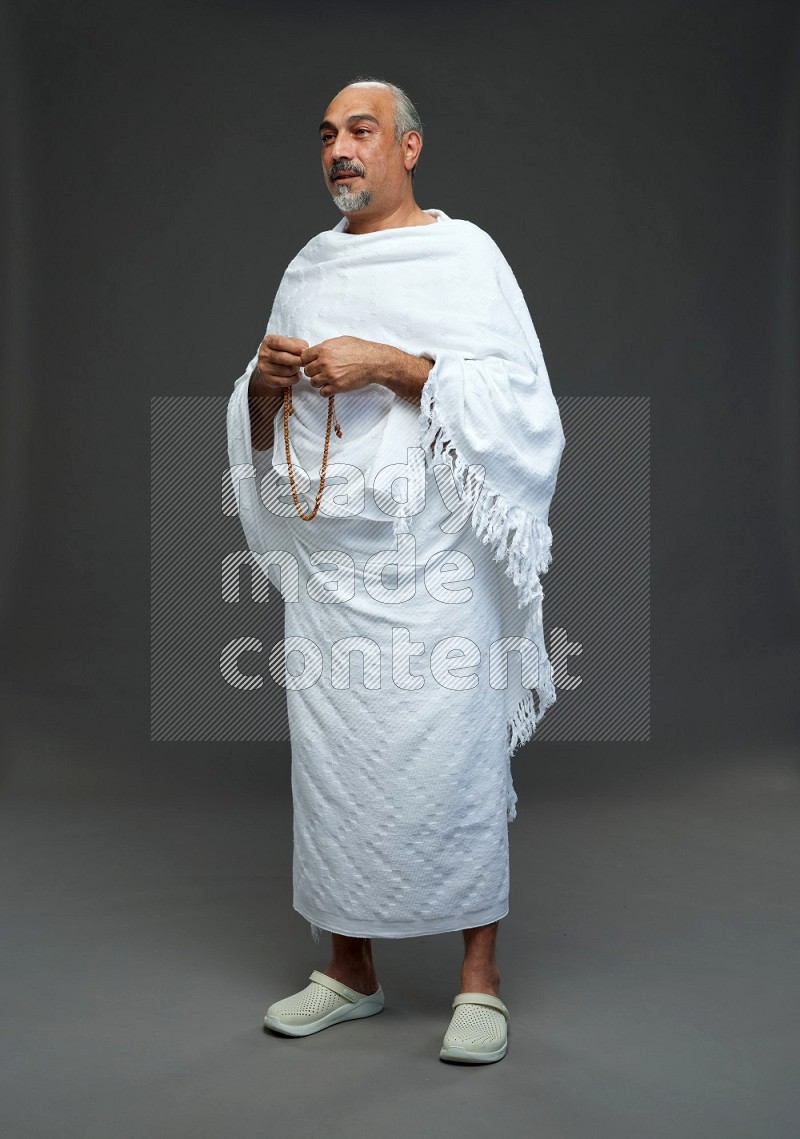 A man wearing Ehram Standing holding rosary on gray background