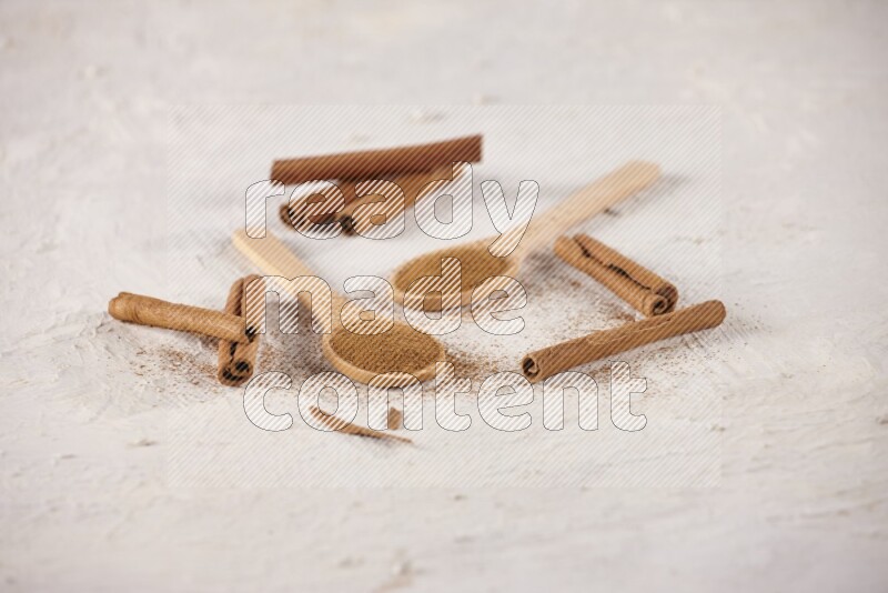 Two wooden spoons full of cinnamon powder with cinnamon sticks on white background