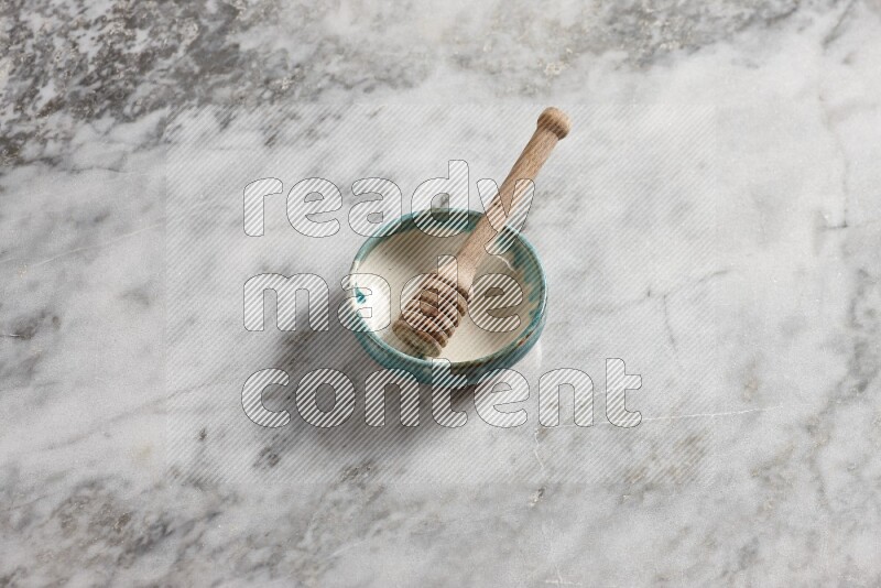 Multicolored pottery bowl with wooden honey dipper in it on grey marble background