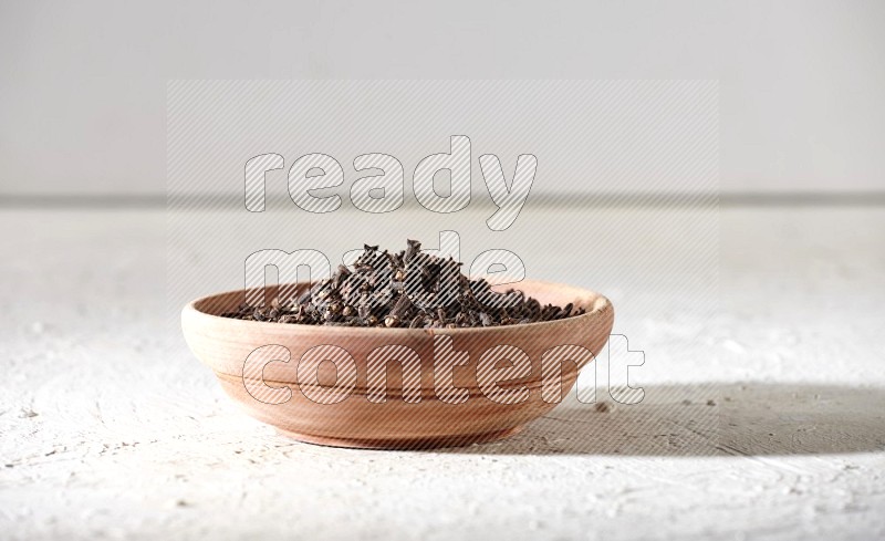 A wooden bowl full of cloves on a white flooring