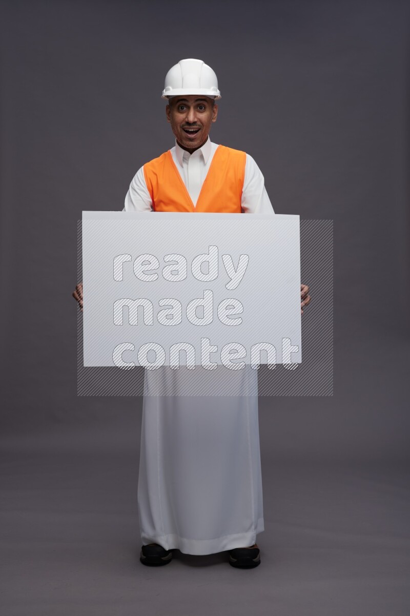 Saudi man wearing thob with engineer vest standing holding board on gray background