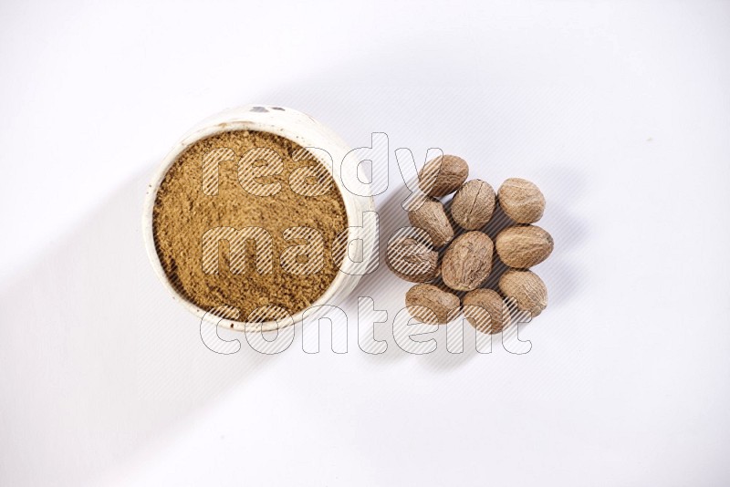 A beige pottery bowl full of nutmeg powder with the seeds beside it on a white flooring in different angles