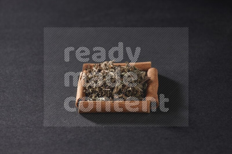 أربعة من أعواد القرفة مكونة شكل مربع بداخلها ريحان مجفف علي خلفية سوداء