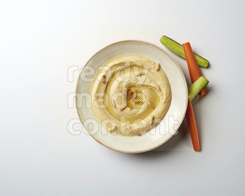 Hummus in a pottry plate garnished with pine nuts on a white background