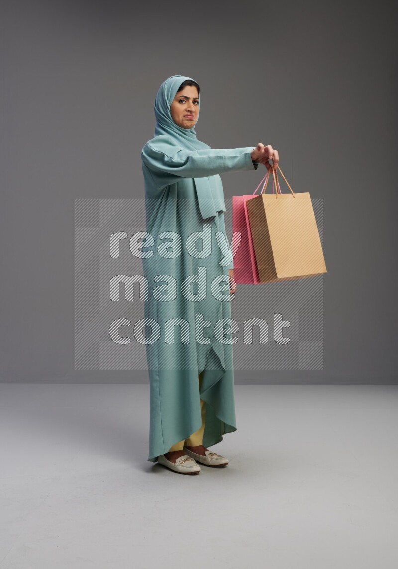 Saudi Woman wearing Abaya standing holding shopping bag on Gray background