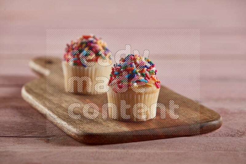 Vanilla mini cupcake topped with sprinkles on a wooden board