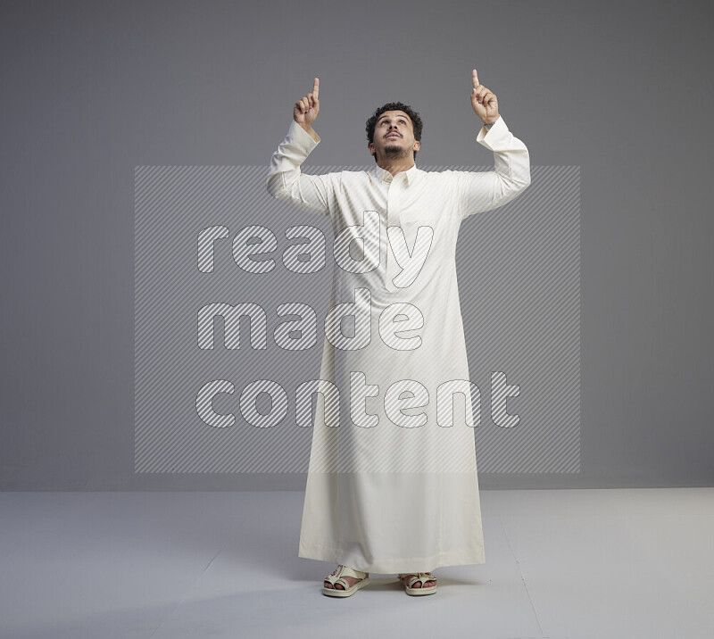 A Saudi man standing wearing thob interacting with the camera on gray background