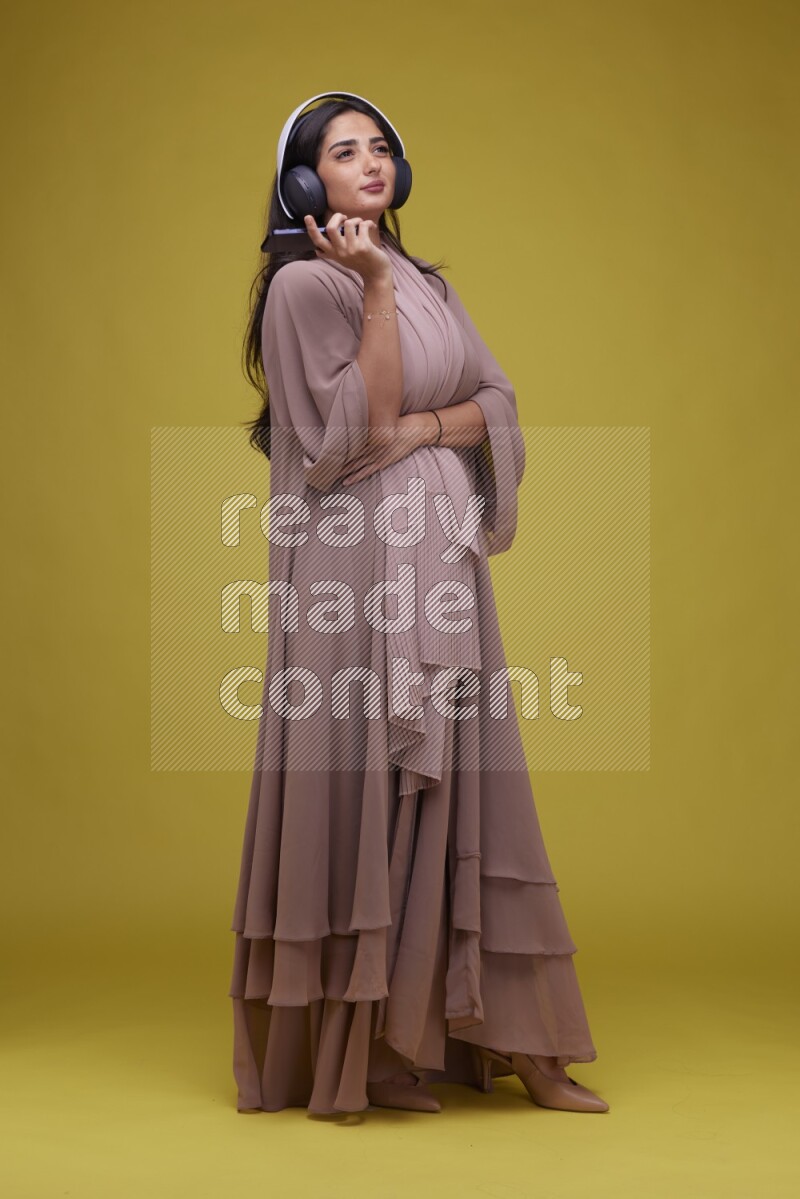 A Saudi woman Listing to Music on a Yellow Background wearing Brown Abaya