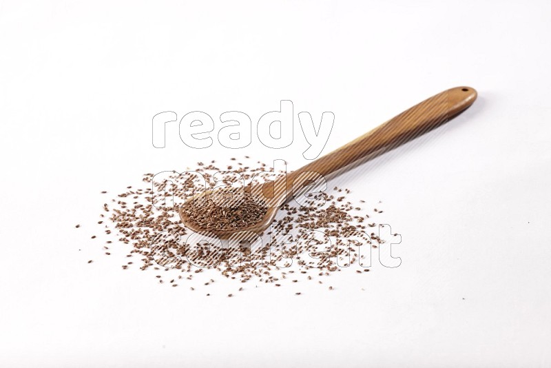 A wooden ladle full of flax seeds on a white flooring