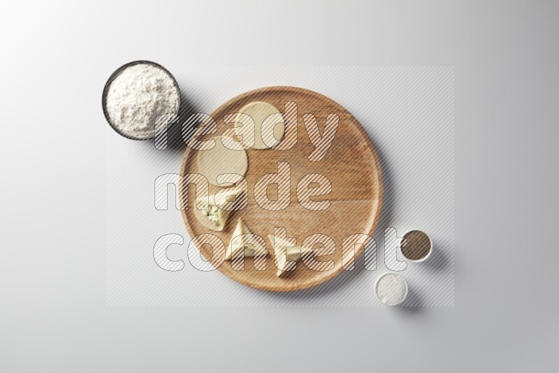two closed sambosas and one open sambosa filled with cheese while flour, salt, and black pepper aside in a wooden dish on a white background