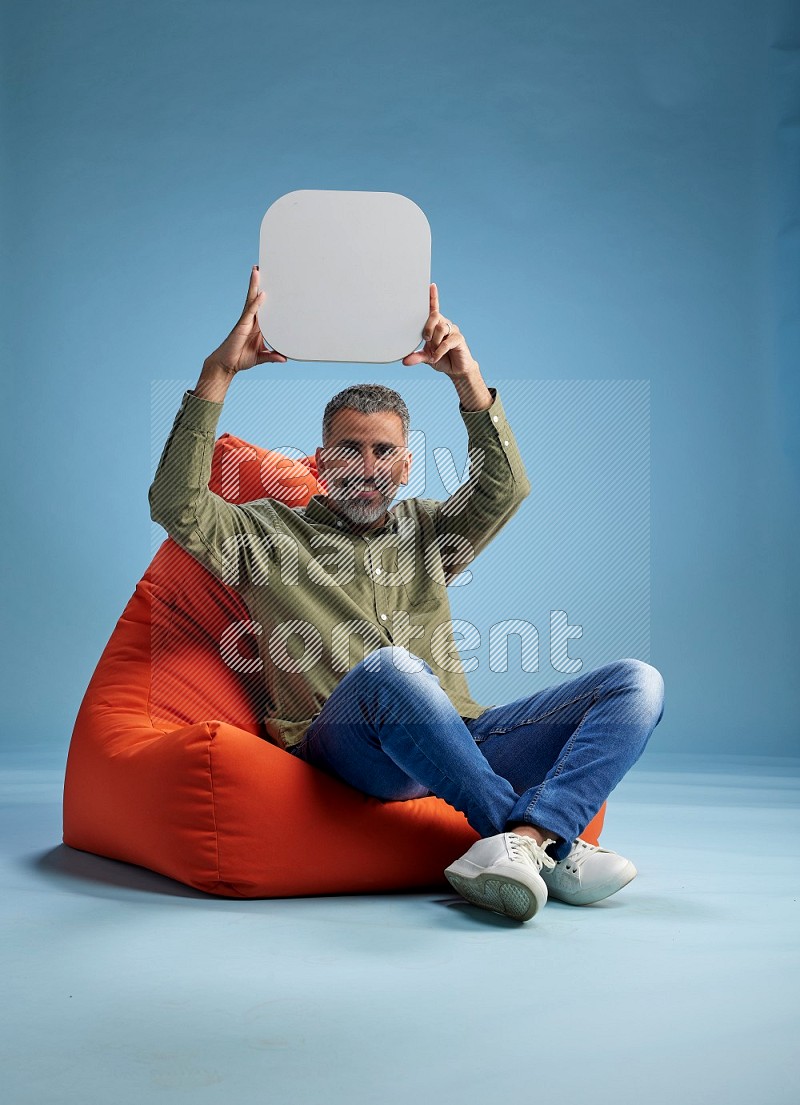 A man sitting on a orange beanbag and holding social media sign