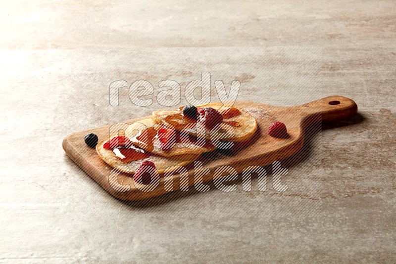 Three stacked mixed berries pancakes on a wooden board on beige background