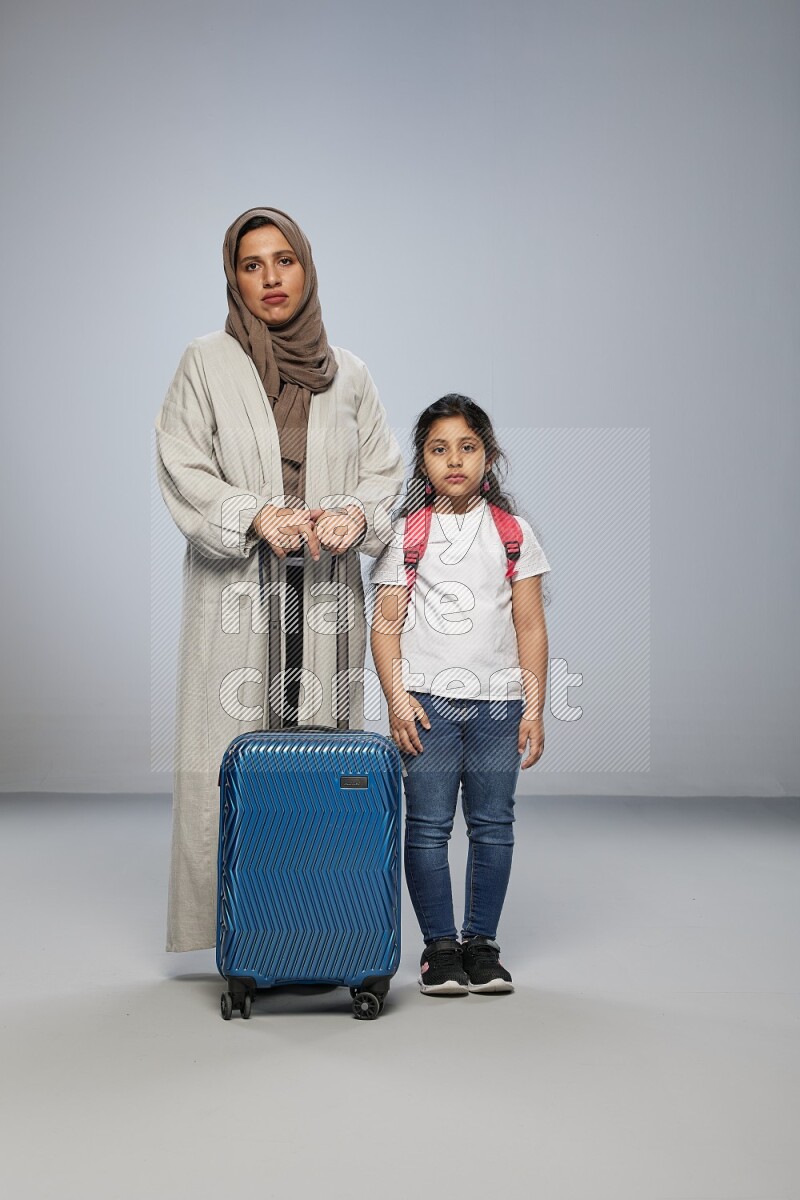 Mom and daughter standing pulling a carry-on bag on gray background