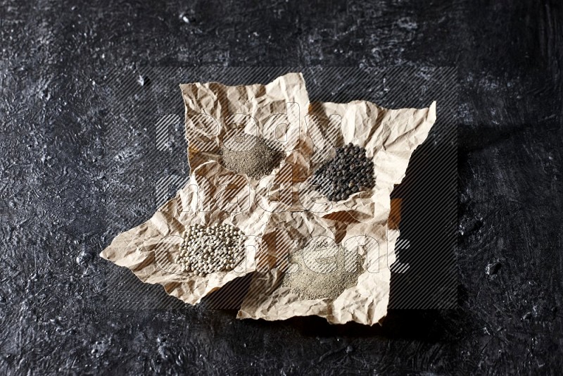 Crumpled pieces of paper full of black and white pepper beads and powder on a textured black flooring