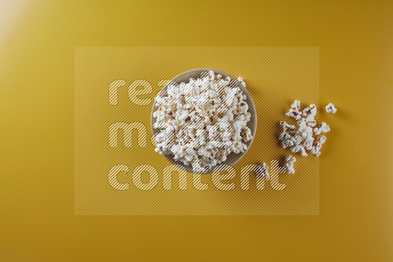 A multicolored ceramic plate full of popcorn with popcorn beside it on a yellow background in different angles