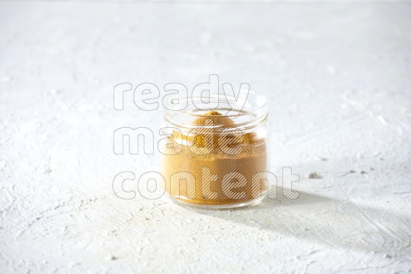 وعاء زجاجي ممتلئ ببودرة الكركم على خلفية بيضاء