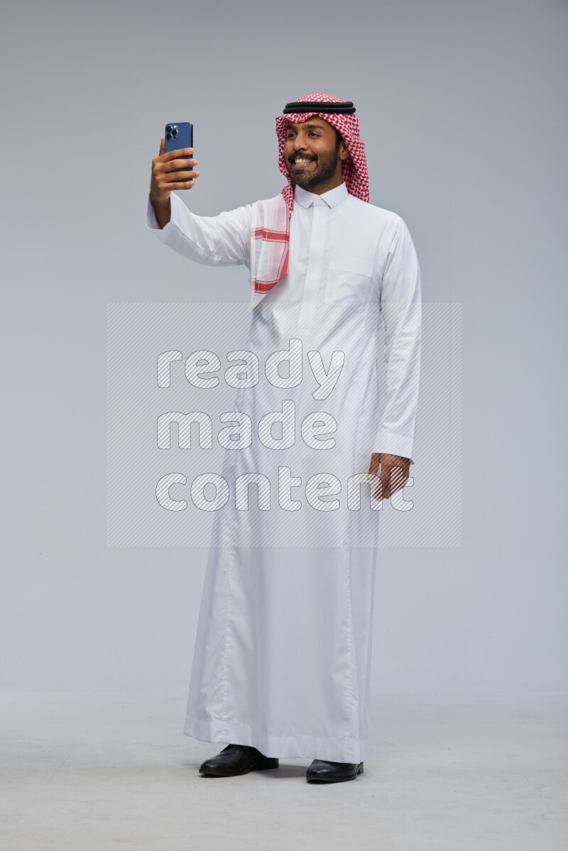 Saudi man Wearing Thob and shomag standing taking selfie on Gray background