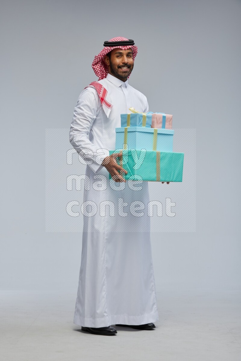 Saudi man Wearing Thob and shomag standing holding gift box on Gray background