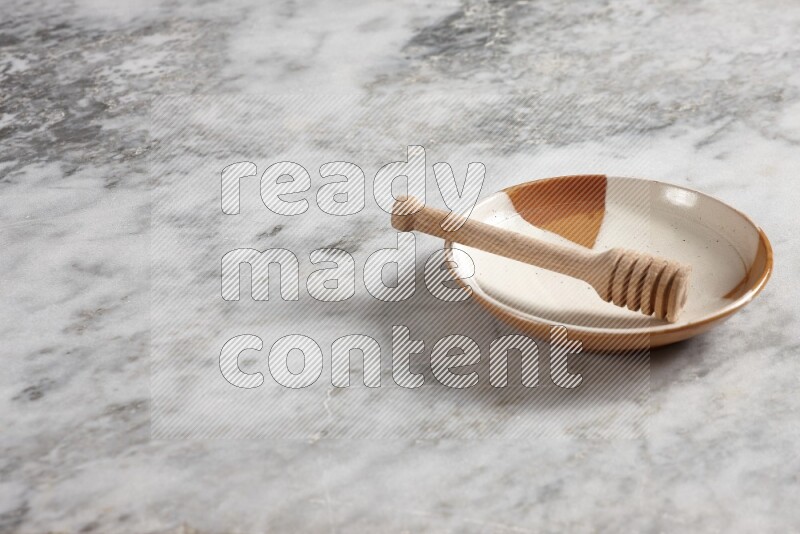 Multicolored pottery plate with wooden honey dipper in it on grey marble background