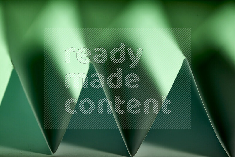 A close-up abstract image showing sharp geometric paper folds in green gradients