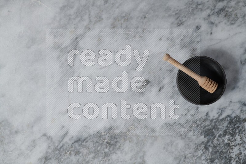 وعاء فخاري أسود مع ملعقة عسل خشبية بداخله على خلفية من الرخام الرمادي