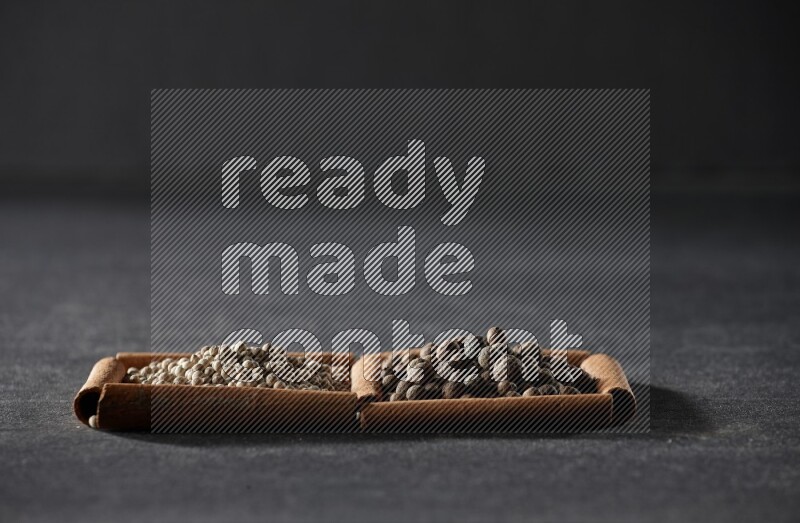 مربعان من أعواد القرفة ممتلئان بحبوب الفلفل الأبيض وحبوب الفلفل الحلو علي خلفية سوداء