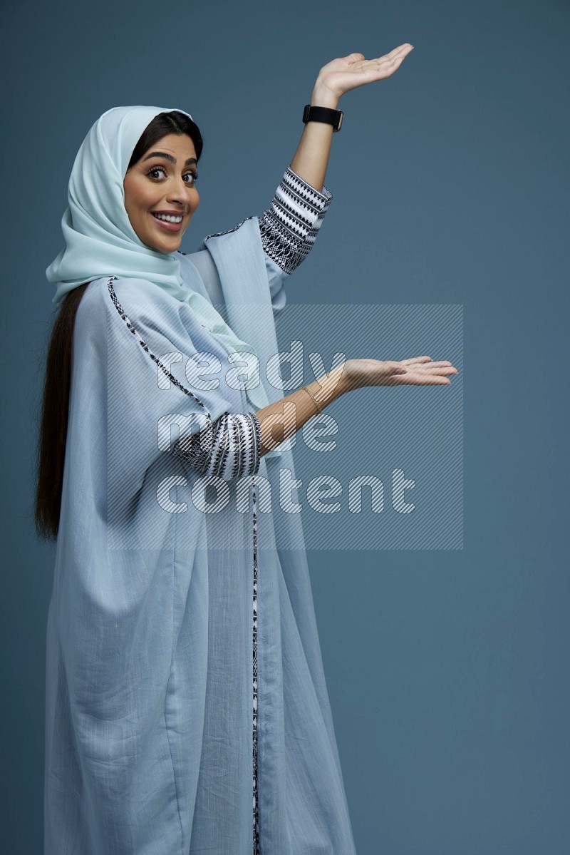 A Saudi woman pointing in a blue background wearing a Blue abaya
