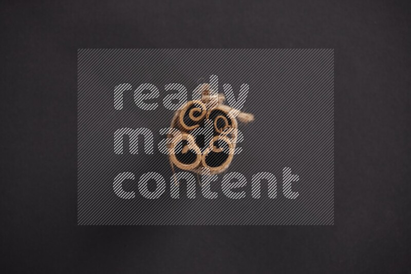 4 Cinnamon sticks stacked and bounded on black flooring