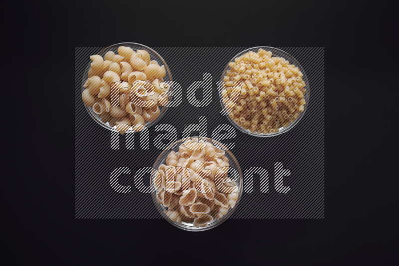 Different pasta types in glass bowls on black background