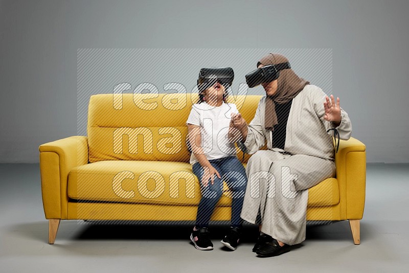 A girl and her mother sitting playing with VR on gray background