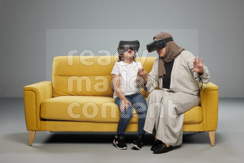 A girl and her mother sitting playing with VR on gray background