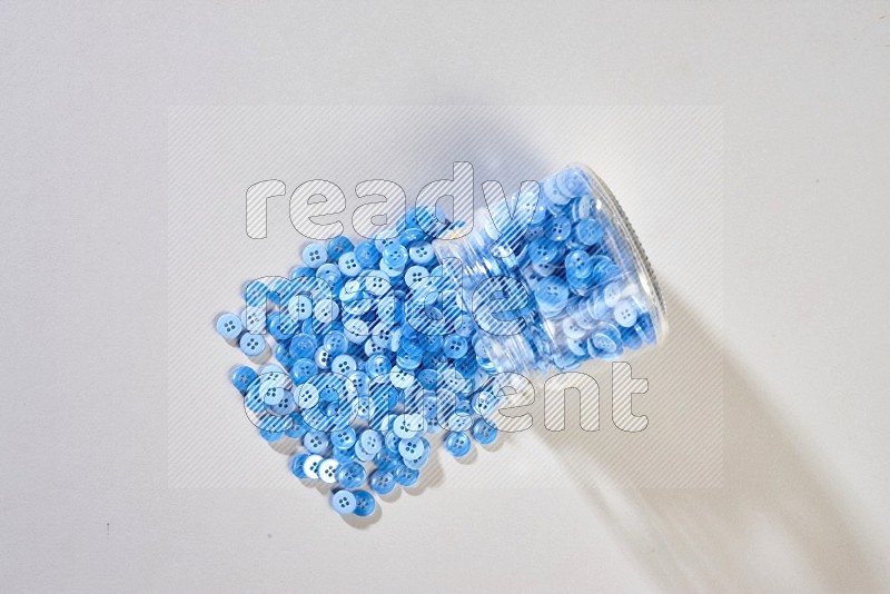 A glass jar full of colored buttons on grey background