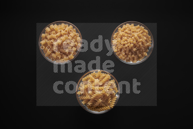 Different pasta types in glass bowls on black background