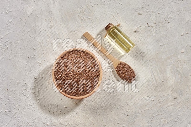 وعاء خشبي ومعلقة خشبية مليئان بحبوب بذر الكتان مع زجاجة من زيت بذر الكتان علي خلفية بيضاء