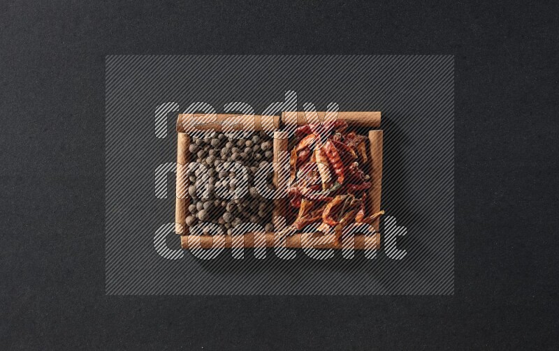 مربعان من أعواد القرفة ممتلئان بالفلفل الحار المجفف وحبوب بهار الفلفل الحلو علي خلفية سوداء