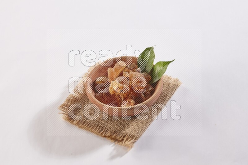 A wooden bowl full of gum arabic on a piece of burlap on white flooring