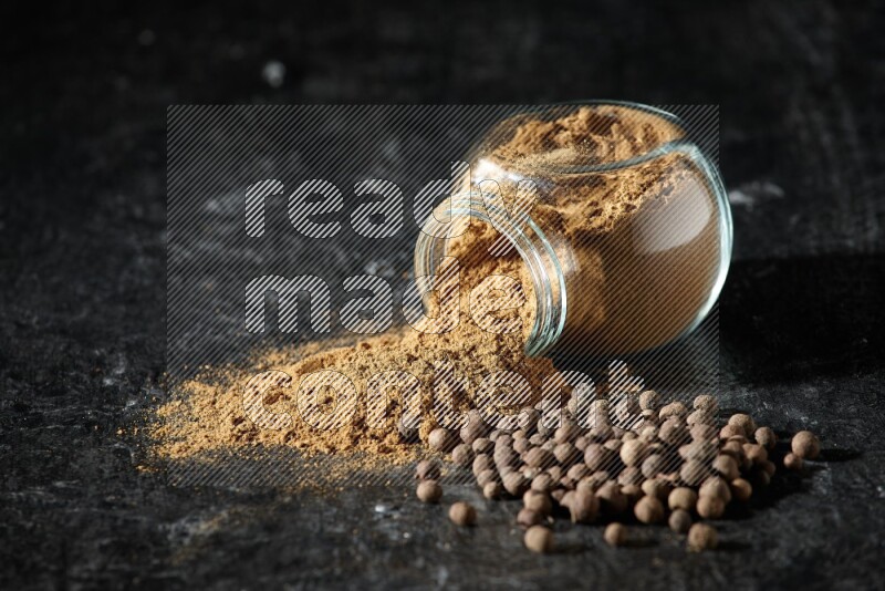 وعاء زجاجي للتوابل مقلوب ممتلئ ببودرة بهار الفلفل الحلو والبودرة تناثرت منه مع الحبوب على خلفية سوداء