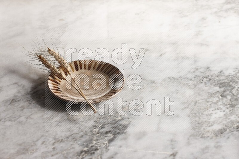 Wheat stalks on multicolored pottery plate on grey marble background