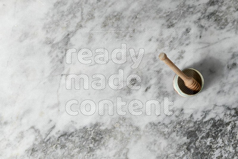 Multicolored Pottery Bowl with wooden honey handle in it, on grey marble flooring, Top View