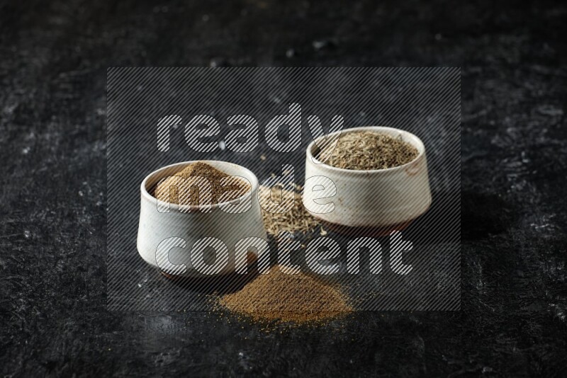 وعاءين بيج، أحدهما ممتلئ ببودرة الكمون والآخر ممتلئ بحبوب الكمون، على خلفية سوداء