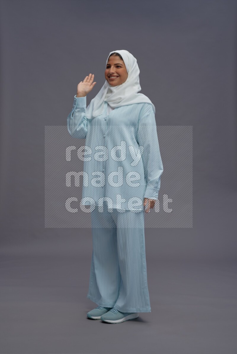 Saudi woman wearing hijab clothes standing interacting with the camera on gray background