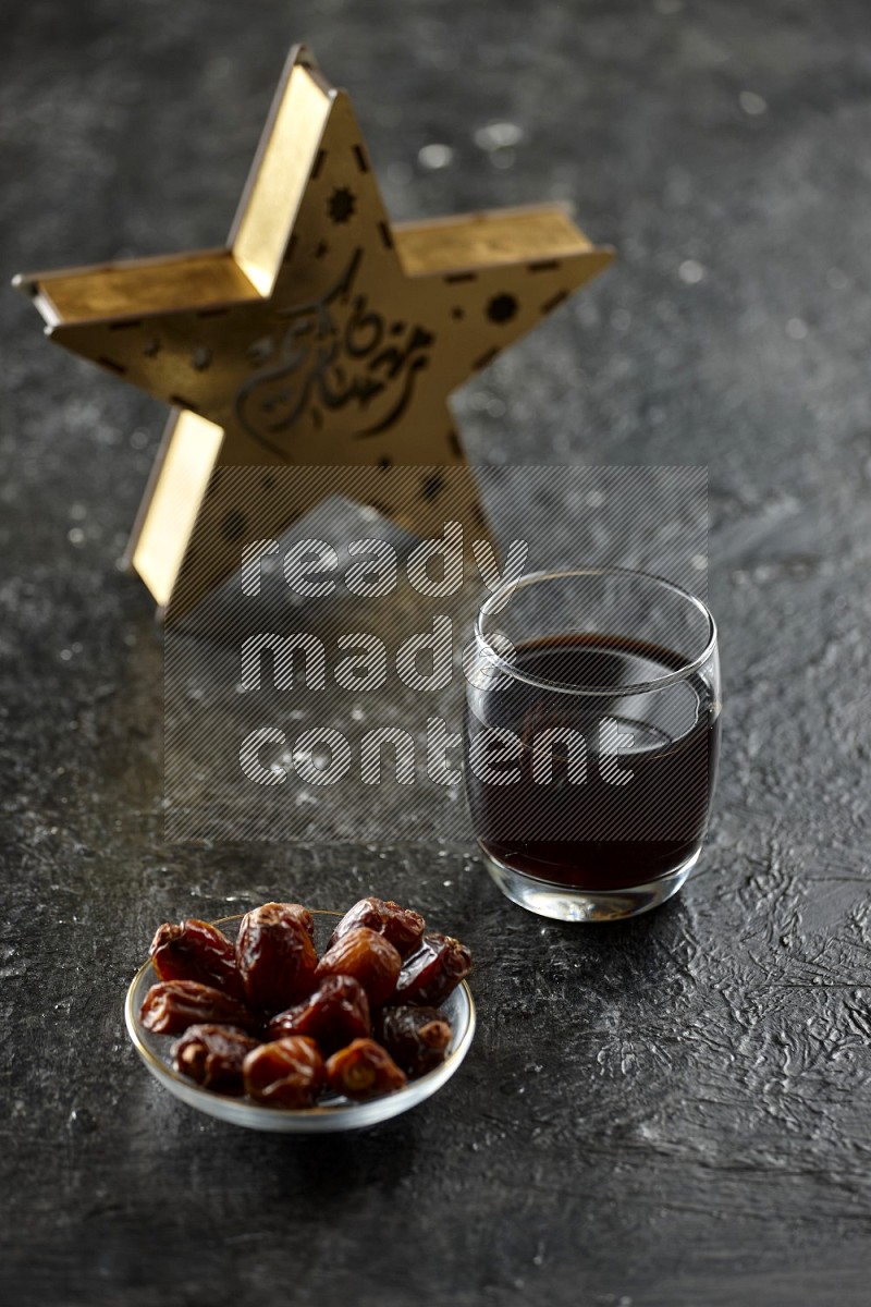 A star lantern with drinks, dates, nuts, prayer beads and quran on textured black background
