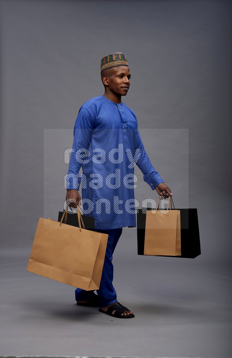 Man wearing Nigerian outfit standing holding shopping bag on gray background