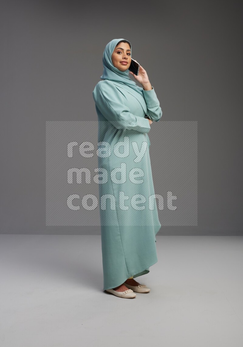 Saudi Woman wearing Abaya standing talking on phone on Gray background