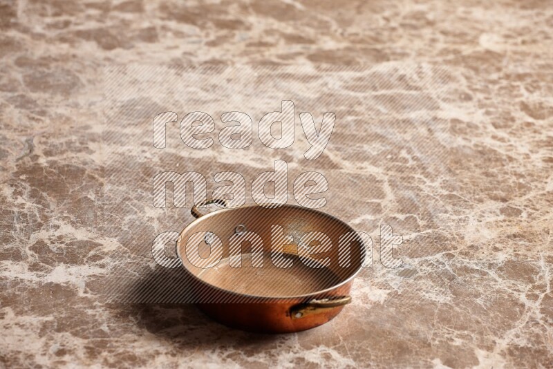 A small copper pan on beige marble background